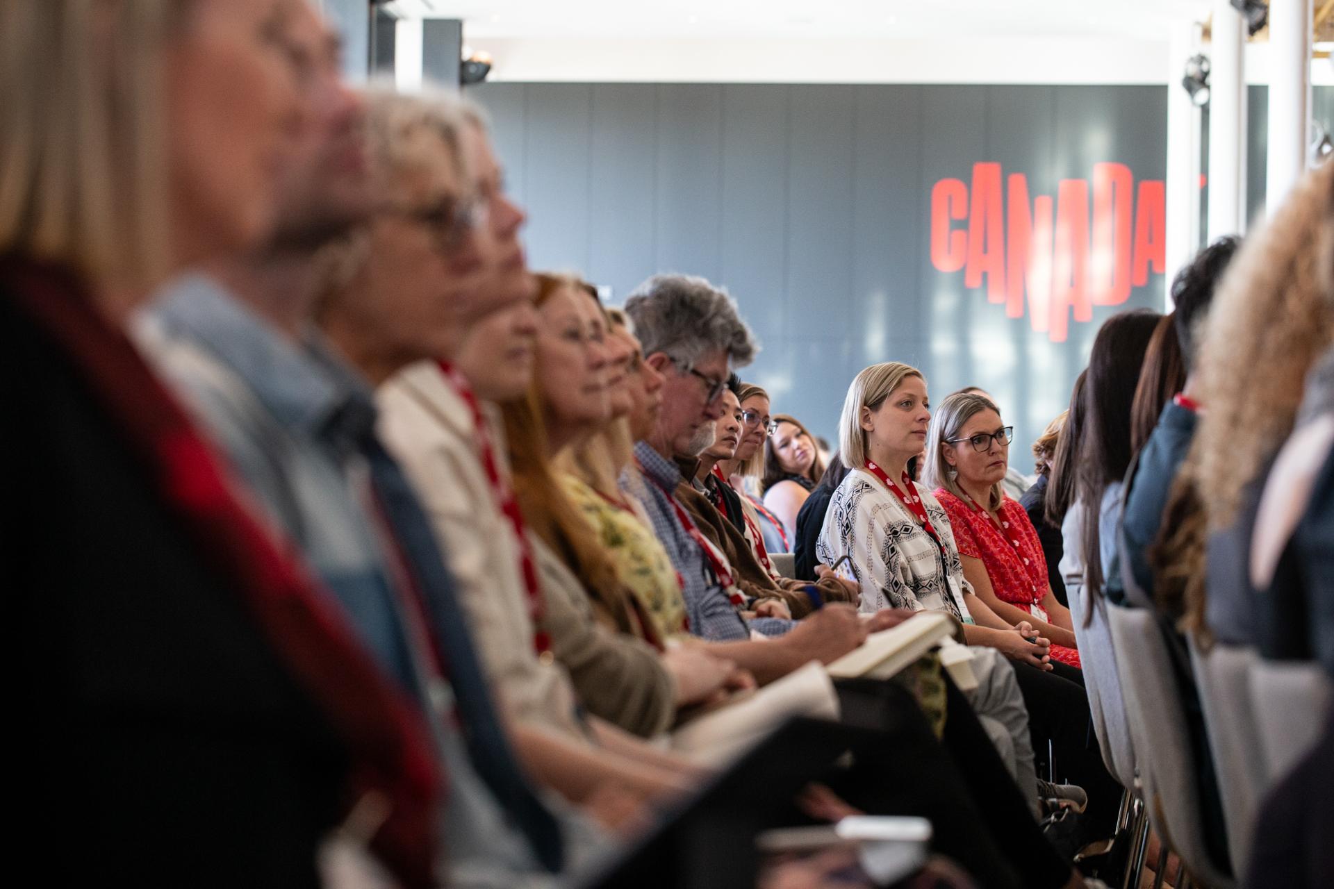 people sitting in crowd at a conference. GoMedia Canada logo blurred in the background